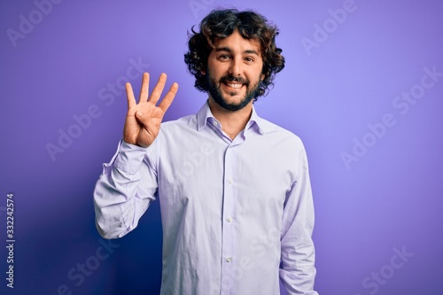 Young handsome business man with beard wearing shirt standing over purple background showing and pointing up with fingers number four while smiling confident and happy.