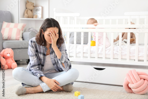 Young woman suffering from postnatal depression near bed with baby at home photo