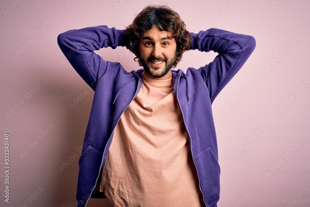 Young handsome sporty man with beard wearing casual sweatshirt over pink background relaxing and stretching, arms and hands behind head and neck smiling happy Young handsome sporty man with beard wearing casual sweatshirt over pink background relaxing and stretching, arms and hands behind head and neck smiling happy