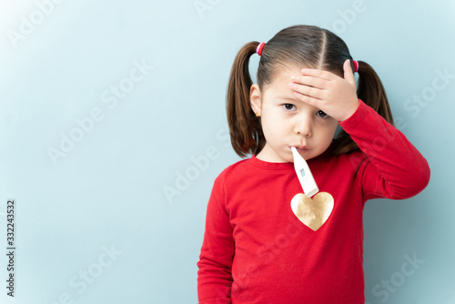 Foto Pretty little girl with ponytails touching her forehead and using a thermometer