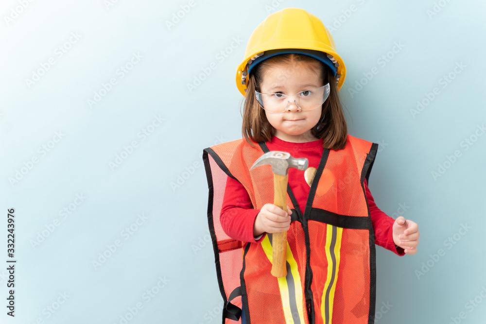 Beautiful little girl aspiring to work in construction and wearing a helmet and a vest and using a hammer