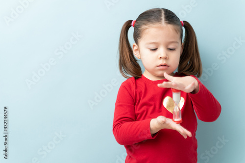 Foto Serious looking little girl looking at a sand timer while practicing self-contro