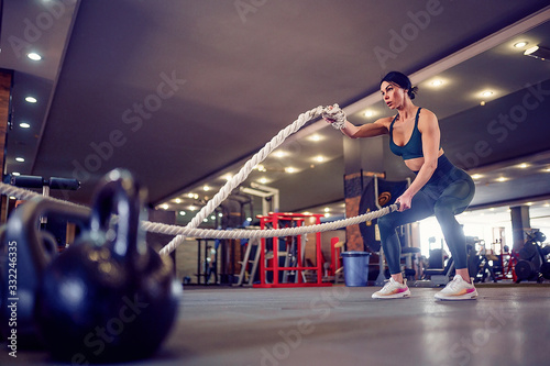 Caucasian fit woman dressed in sportsoutfit working hard with battle ropes at gym. © zamuruev