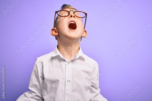 Young little caucasian kid with blue eyes wearing glasses and white shirt over purple background crazy and mad shouting and yelling with aggressive expression and arms raised. Frustration concept.