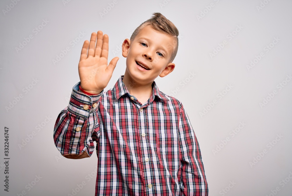 Naklejka premium Young little caucasian kid with blue eyes wearing elegant shirt standing over isolated background Waiving saying hello happy and smiling, friendly welcome gesture