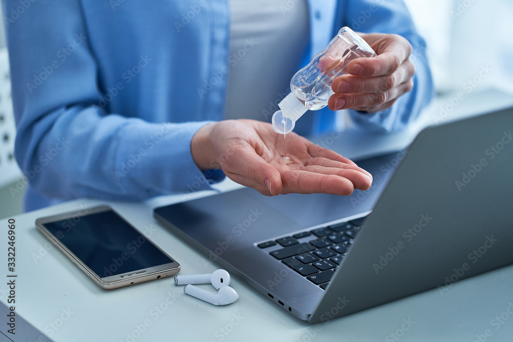 Woman applying an antibacterial antiseptic gel for disinfection and cleaning hands while working at a computer. Protection against viruses, germs and bacteria during coronavirus outbreak - obrazy, fototapety, plakaty 