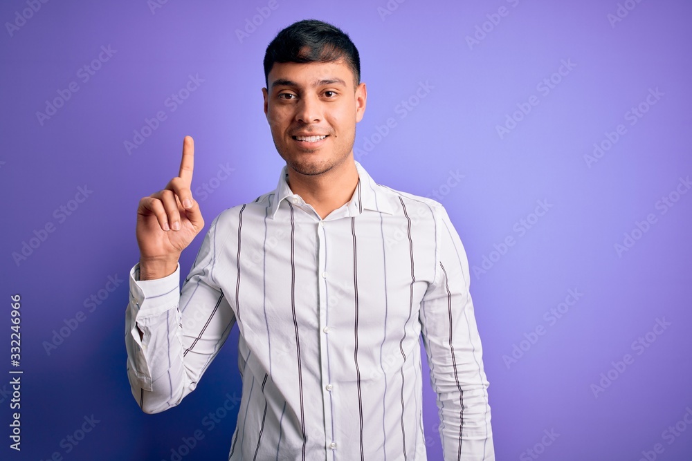 Young handsome hispanic man wearing elegant business shirt standing over purple background pointing finger up with successful idea. Exited and happy. Number one. Young handsome hispanic man wearing elegant business shirt standing over purple background pointing finger up with successful idea. Exited and happy. Number one.