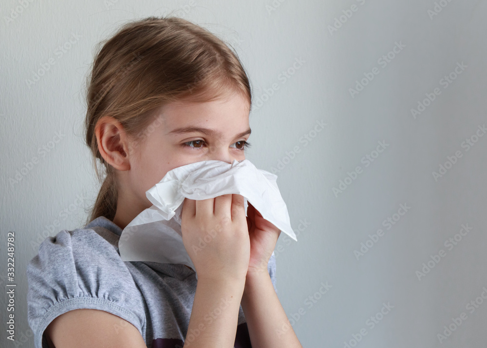 Young girl blowing her nose into a paper handkerchief in front of a white background. Young girl blowing her nose into a paper handkerchief in front of a white background.