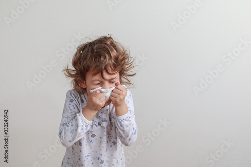 Young girl sneezing into a paper handkerchief in front of a white background.