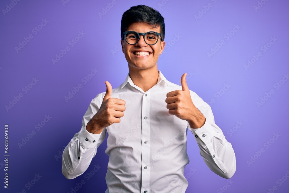 Young handsome business man wearing shirt and glasses over isolated purple background success sign doing positive gesture with hand, thumbs up smiling and happy. Cheerful expression and winner