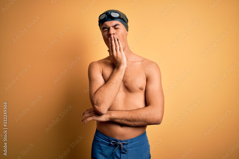 Young handsome man shirtless wearing swimsuit and swim cap over isolated yellow background bored yawning tired covering mouth with hand. Restless and sleepiness.
