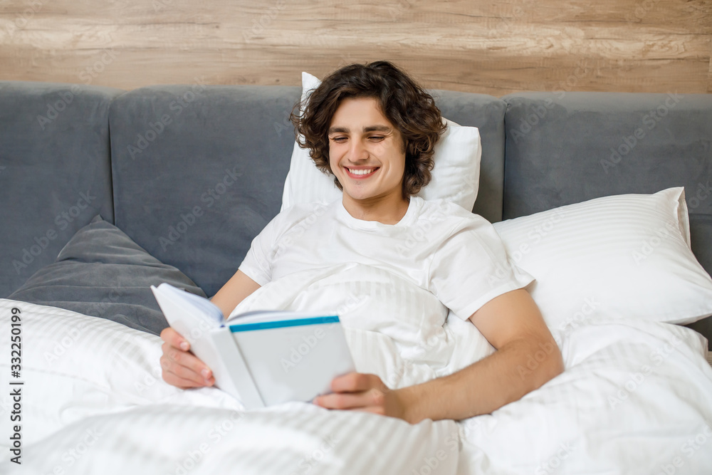 Portrait of young man laying on his bed while reading a book at resting at weekend on his bedroom Portrait of young man laying on his bed while reading a book at resting at weekend on his bedroom