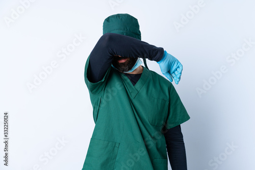 Surgeon man in green uniform over isolated background covering eyes by hands