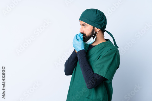 Surgeon man in green uniform over isolated background covering mouth and looking to the side