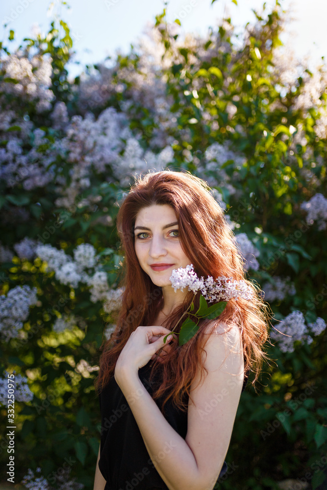Naklejka premium Portrait of woman holding lilac flowers bouquet on blossomig bush background