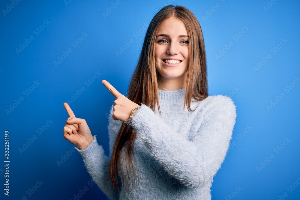 Young beautiful redhead woman wearing casual sweater over isolated blue background smiling and looking at the camera pointing with two hands and fingers to the side.