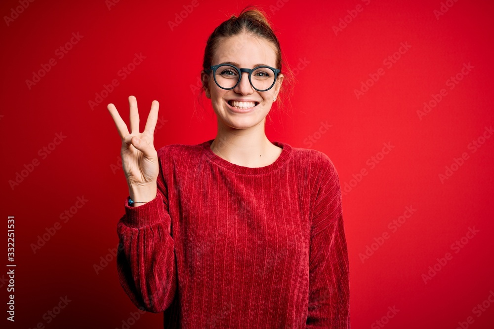 Young beautiful redhead woman wearing casual sweater over isolated red background showing and pointing up with fingers number three while smiling confident and happy. Young beautiful redhead woman wearing casual sweater over isolated red background showing and pointing up with fingers number three while smiling confident and happy.