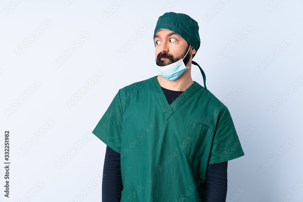 Surgeon man in green uniform over isolated background making doubts gesture looking side