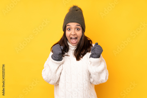 Young woman with winter hat over isolated yellow background celebrating a victory in winner position © luismolinero