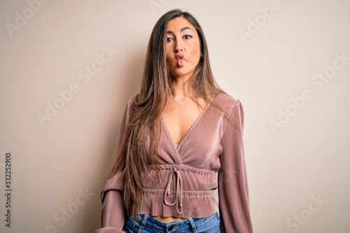Young beautiful brunette elegant woman with long hair standing over isolated background making fish face with lips, crazy and comical gesture. Funny expression.