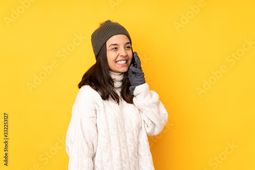 Young woman with winter hat over isolated yellow background keeping a conversation with the mobile phone © luismolinero
