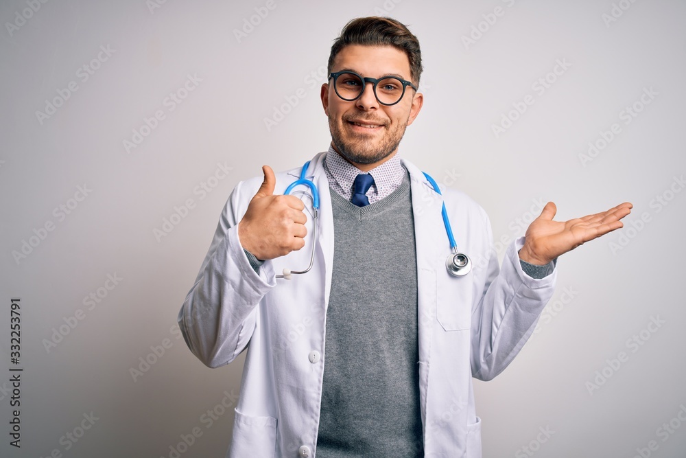 Young doctor man with blue eyes wearing medical coat and stethoscope over isolated background Showing palm hand and doing ok gesture with thumbs up, smiling happy and cheerful