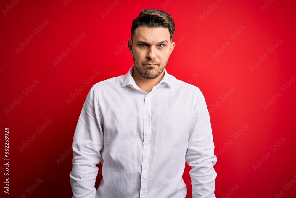 Young business man with blue eyes wearing elegant shirt standing over red isolated background skeptic and nervous, frowning upset because of problem. Negative person. Young business man with blue eyes wearing elegant shirt standing over red isolated background skeptic and nervous, frowning upset because of problem. Negative person.