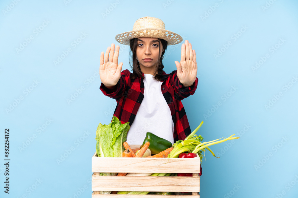 Young farmer Woman holding fresh vegetables in a wooden basket making stop gesture and disappointed