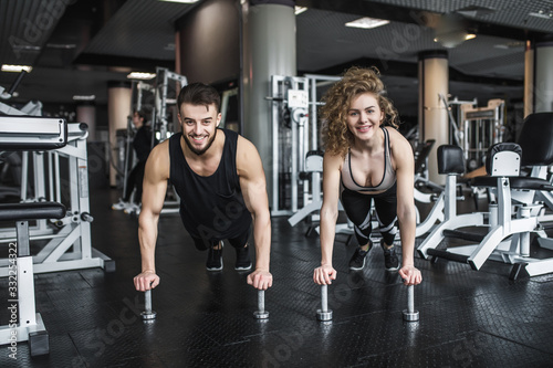 Motivated young blond woman and man trainer in middle of workout  standing in plank with dumbbells