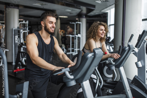 Attractive young woman and her trainer running on treadmill in gym. Slim girl jogging in fitness club, smiling at camera. Healthy lifestyle concept, cardio training