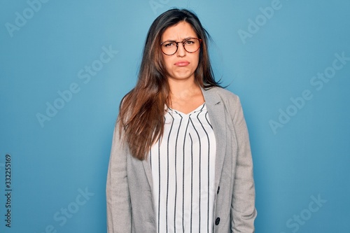 Young hispanic business woman wearing glasses standing over blue isolated background depressed and worry for distress, crying angry and afraid. Sad expression. © Krakenimages.com