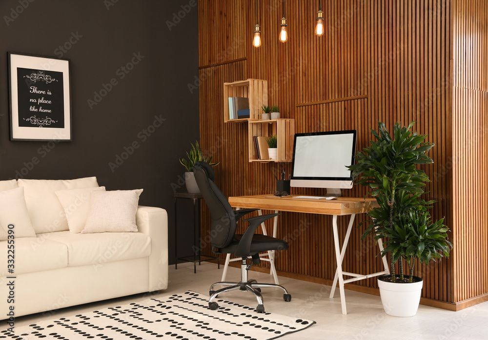 Obraz premium Comfortable workplace with computer near wooden wall in stylish room interior. Home office design
