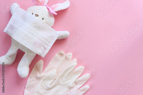 White toy rabbit with white mask and gloves on isolated pink background. Happy easter concept with coronavirus risk. Canceled easter.