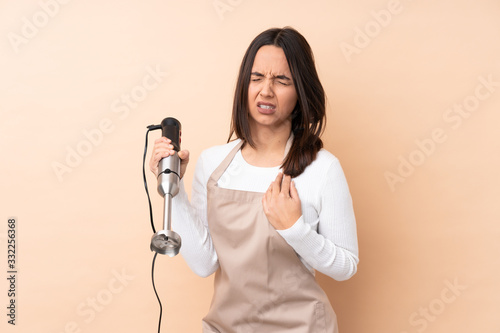 Young brunette girl using hand blender over isolated background having a pain in the heart