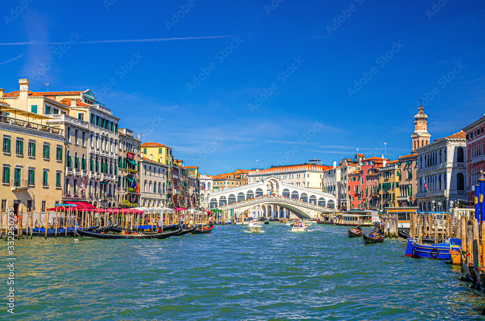 Venice cityscape with Rialto Bridge across Grand Canal waterway, Venetian architecture colorful buildings, gondolas, boats, vaporettos docked and sailing Canal Grande. Veneto Region, Northern Italy.