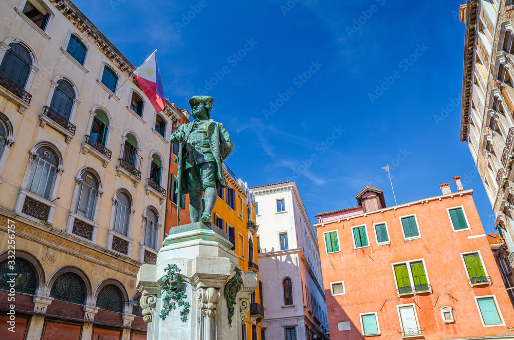 Carlo Goldoni Monument on Campo Bortolomio square between colorful buildings, blue sky background, Venice city, Veneto Region, Northern Italy