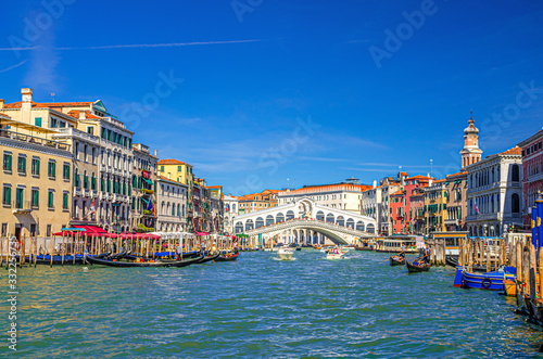 Venice cityscape with Rialto Bridge across Grand Canal waterway, Venetian architecture colorful buildings, gondolas, boats, vaporettos docked and sailing Canal Grande. Veneto Region, Northern Italy.