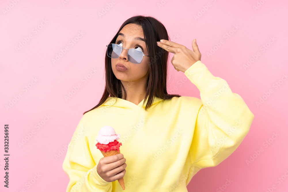 Young brunette girl holding a cornet ice cream over isolated pink background with problems making suicide gesture Young brunette girl holding a cornet ice cream over isolated pink background with problems making suicide gesture