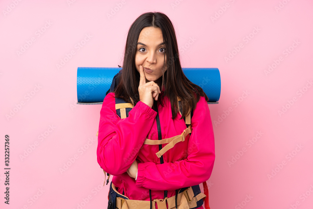 Young mountaineer girl with a big backpack over isolated pink background and looking front Young mountaineer girl with a big backpack over isolated pink background and looking front