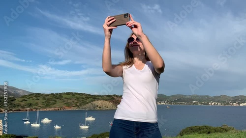 Happy blonde woman tourist taking landscape photos of the sea from hill top
