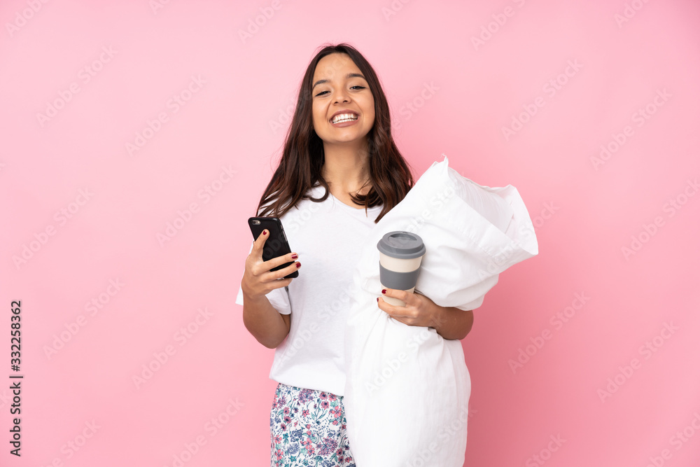 Young woman in pajamas isolated on pink background holding coffee to take away and a mobile Young woman in pajamas isolated on pink background holding coffee to take away and a mobile