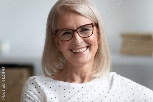 Close up head shot portrait of smiling attractive middle aged woman in eyeglasses. Happy older female teacher with toothy smile recording educational video, giving remote professional consultation.