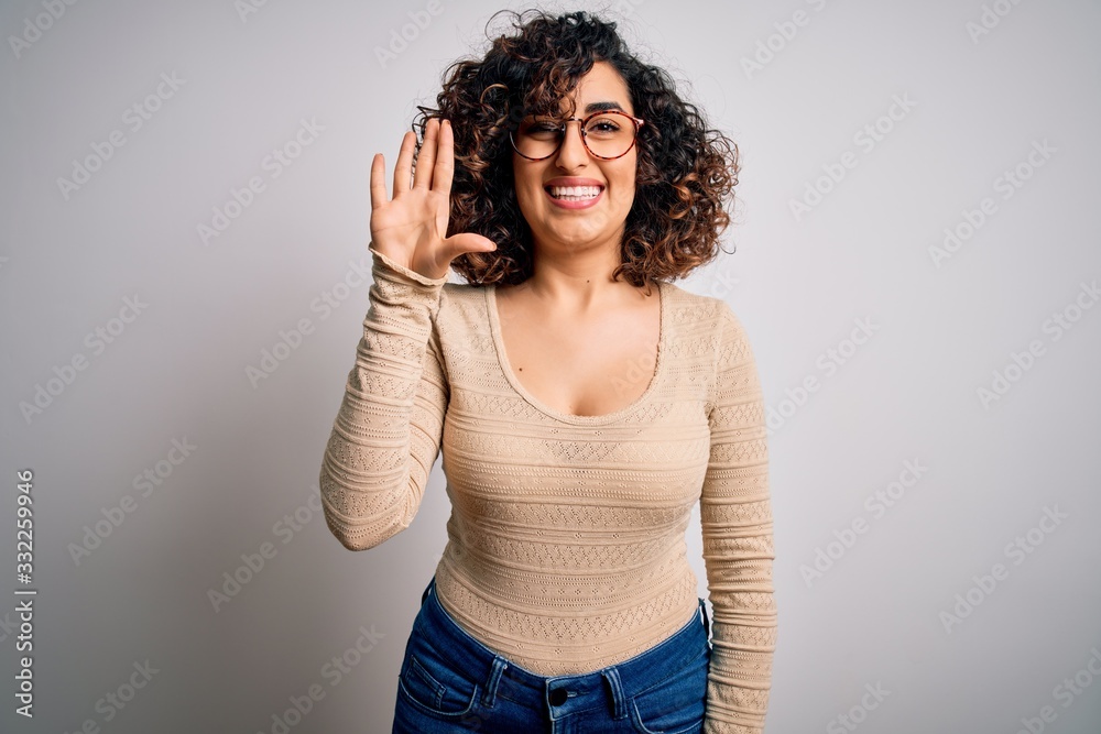 Young beautiful curly arab woman wearing casual t-shirt and glasses over white background showing and pointing up with fingers number five while smiling confident and happy. Young beautiful curly arab woman wearing casual t-shirt and glasses over white background showing and pointing up with fingers number five while smiling confident and happy.