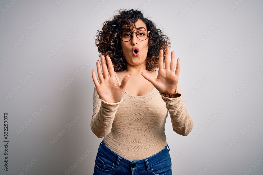 Young beautiful curly arab woman wearing casual t-shirt and glasses over white background Moving away hands palms showing refusal and denial with afraid and disgusting expression. Stop and forbidden. Young beautiful curly arab woman wearing casual t-shirt and glasses over white background Moving away hands palms showing refusal and denial with afraid and disgusting expression. Stop and forbidden.
