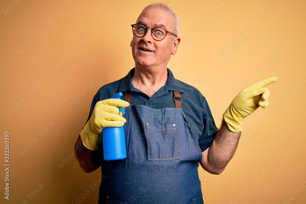 Middle age hoary cleaner man cleaning wearing apron and gloves using sprayer very happy pointing with hand and finger to the side Middle age hoary cleaner man cleaning wearing apron and gloves using sprayer very happy pointing with hand and finger to the side