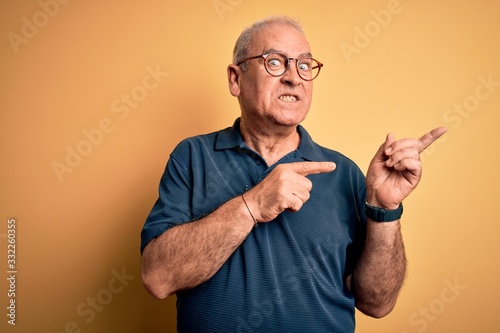 Middle age handsome hoary man wearing casual polo and glasses over yellow background Pointing aside worried and nervous with both hands, concerned and surprised expression