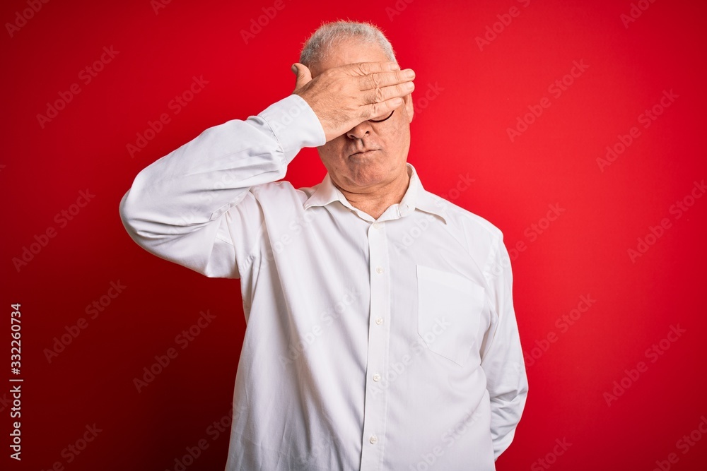 Middle age handsome hoary man wearing casual shirt and glasses over red background covering eyes with hand, looking serious and sad. Sightless, hiding and rejection concept Middle age handsome hoary man wearing casual shirt and glasses over red background covering eyes with hand, looking serious and sad. Sightless, hiding and rejection concept