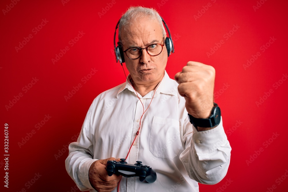 Middle age handsome hoary gamer man playing video game using joystick and headphones annoyed and frustrated shouting with anger, crazy and yelling with raised hand, anger concept Middle age handsome hoary gamer man playing video game using joystick and headphones annoyed and frustrated shouting with anger, crazy and yelling with raised hand, anger concept