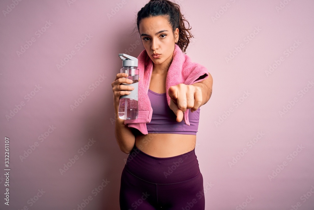 Young beautiful sportswoman with curly hair doing sport drinking bottle of water using towel pointing with finger to the camera and to you, hand sign, positive and confident gesture from the front Young beautiful sportswoman with curly hair doing sport drinking bottle of water using towel pointing with finger to the camera and to you, hand sign, positive and confident gesture from the front