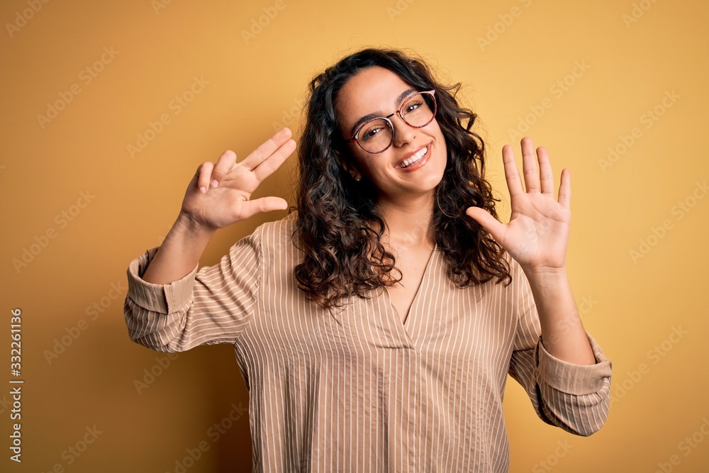 Beautiful woman with curly hair wearing striped shirt and glasses over yellow background showing and pointing up with fingers number eight while smiling confident and happy. Beautiful woman with curly hair wearing striped shirt and glasses over yellow background showing and pointing up with fingers number eight while smiling confident and happy.